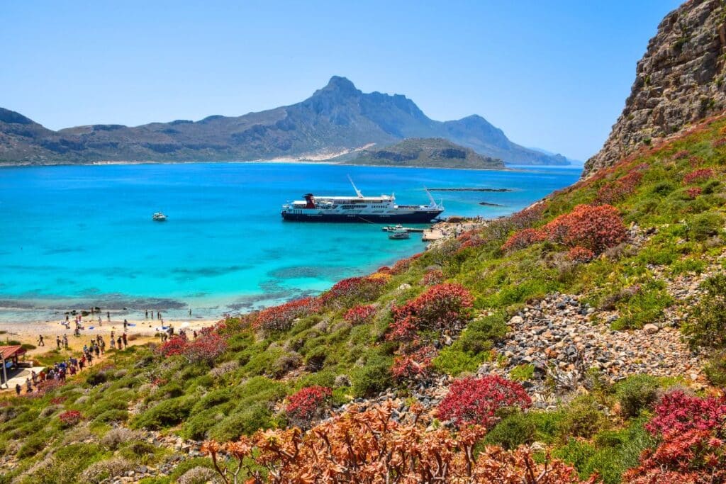 Read and green shrubs line a rocky hillside on Gramvousa island Crete with the sea in the distance