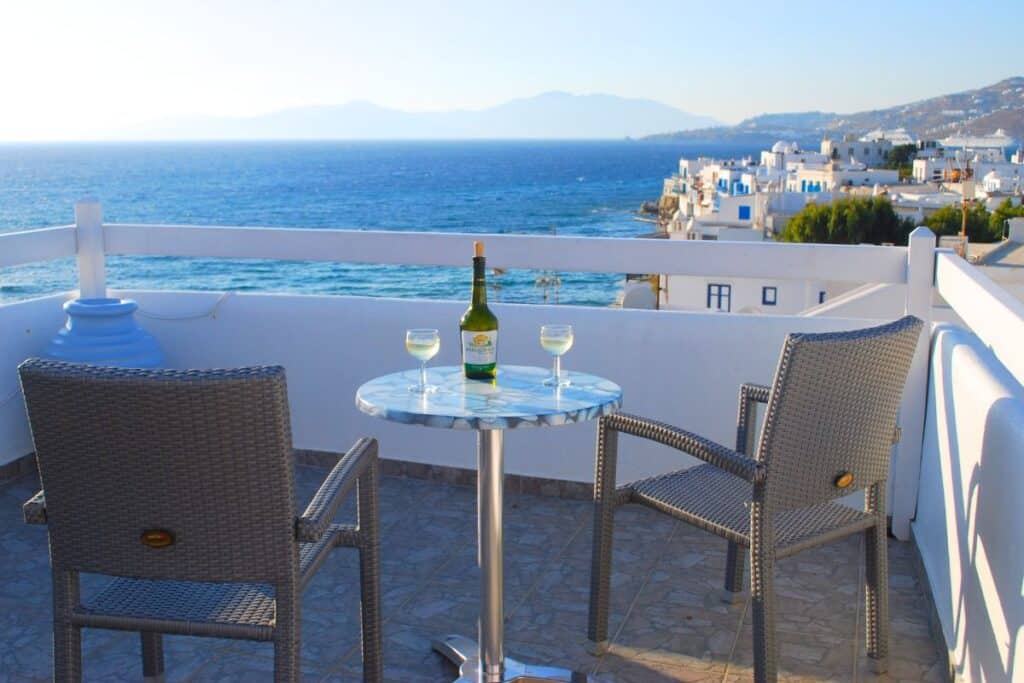 A balcony overlooking the sea with two chairs and a small table with wine glasses on it