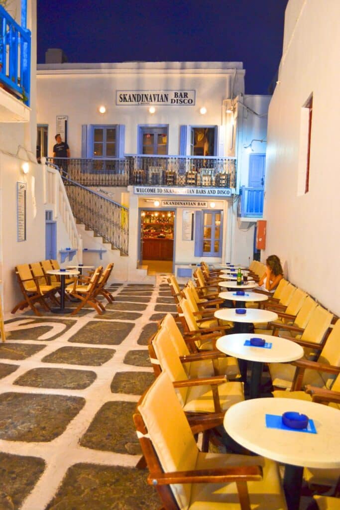 Empty cafe tables line a cobbled alleyway at night in Mykonos greece