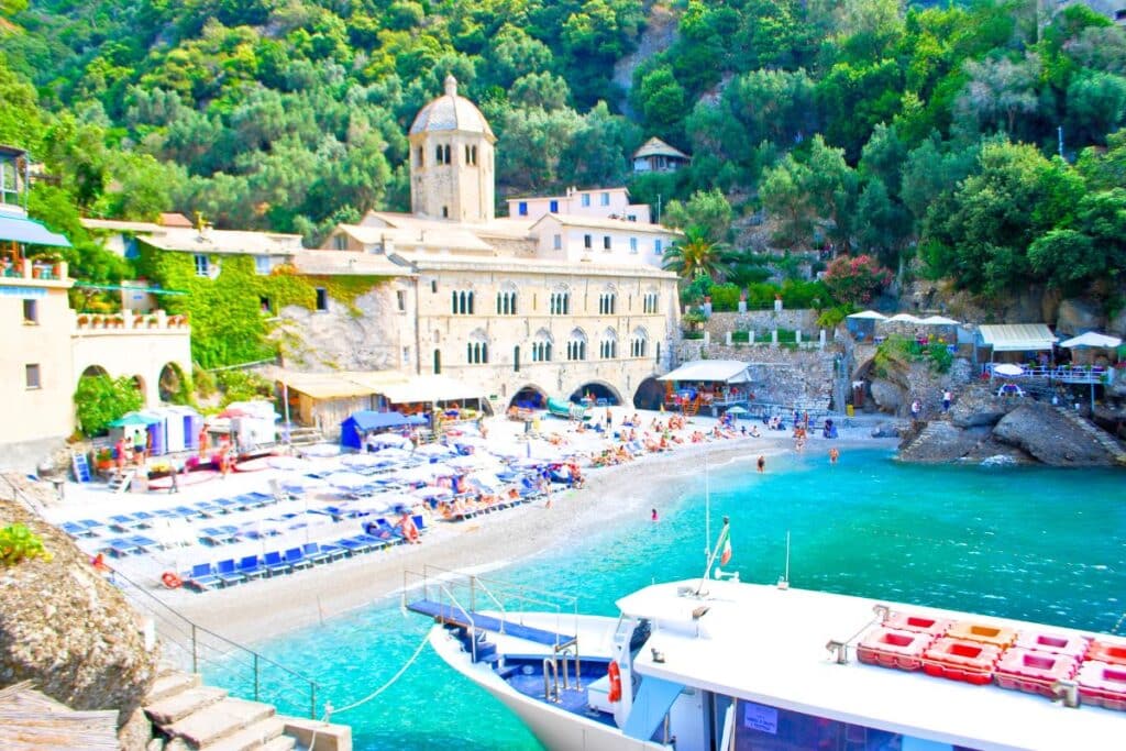 A stone monastery on a white sand beach along a turquoise sea in Italy