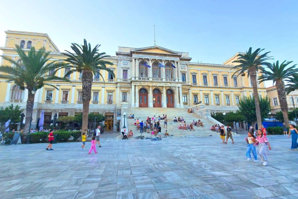 The neoclassical town hall on Syros greece with people sitting on the large staircase and a marble courtyard
