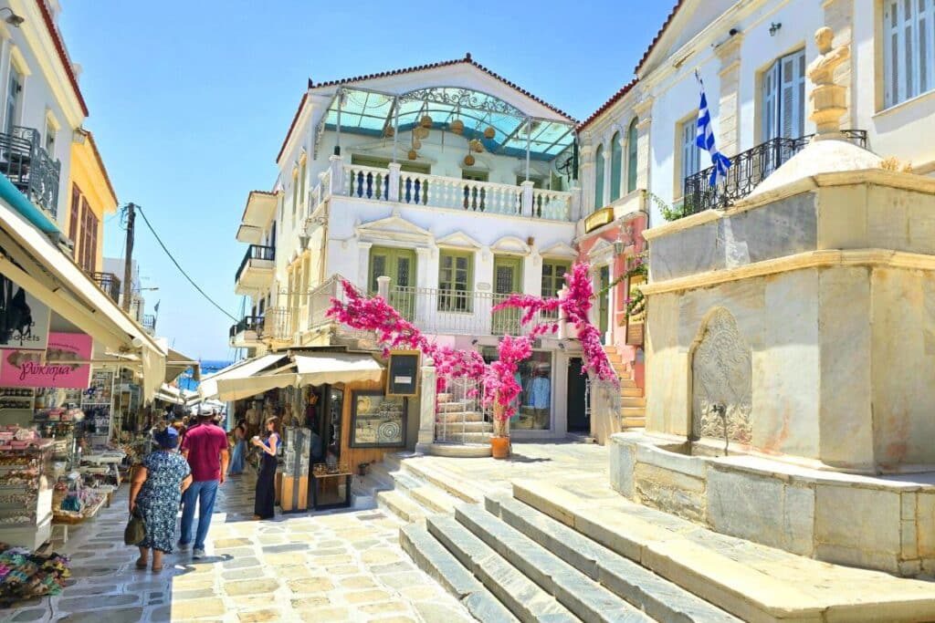 Pink flowers on a vine hanging over shops on a cobbled street in Tinos